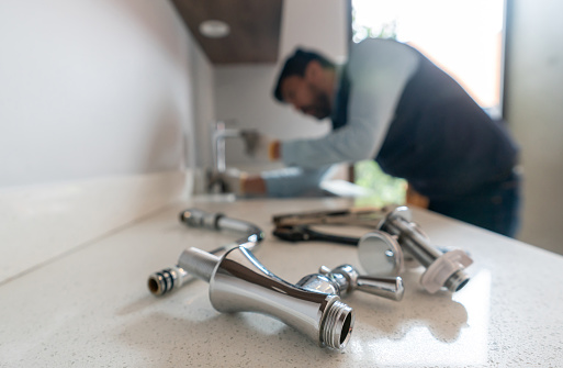 Latin American plumber fixing a leak in the kitchen sink of a house - focus on his tools