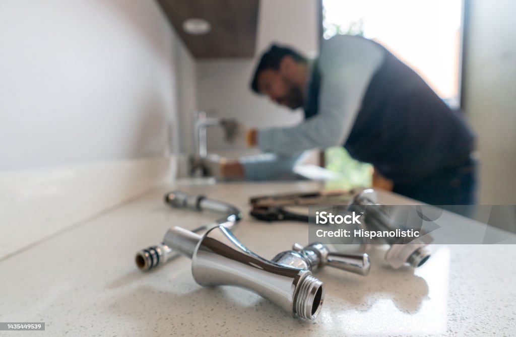 Plumber fixing a leak in the kitchen sink of a house Latin American plumber fixing a leak in the kitchen sink of a house - focus on his tools Plumber Stock Photo