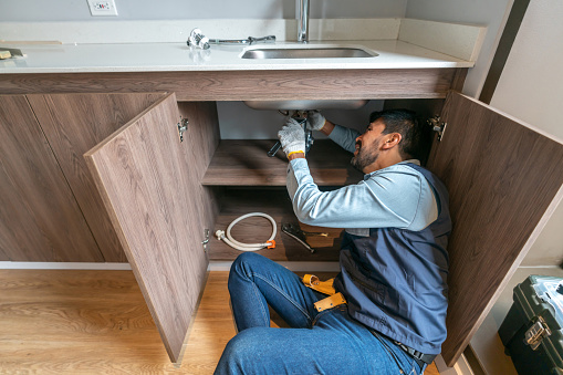 Latin American plumber fixing a leak in the kitchen sink of a house - domestic life