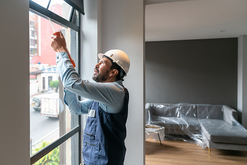 Repairman fixing a leak on a window at an apartment using a silicone gun