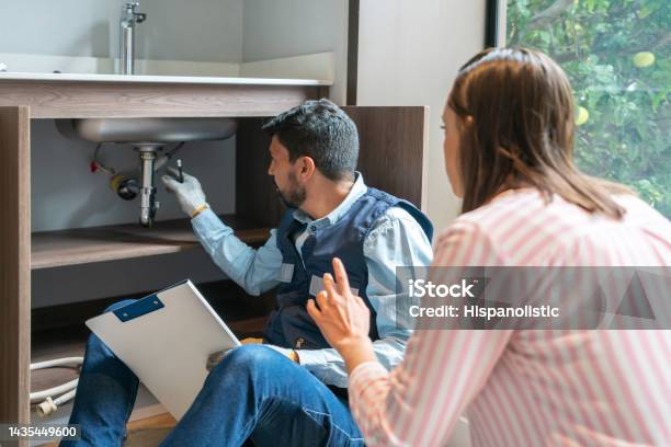 Plumber Explaining To A Client The Problem With Her Kitchen Sink Stock Photo - Download Image Now
