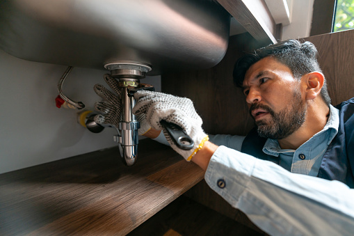 Latin American plumber fixing a leak in the kitchen sink of a house - domestic life