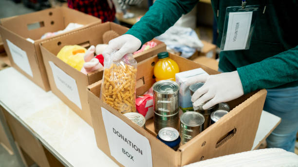 Unrecognizable volunteer organizing donations in boxes wearing protective gloves Unrecognizable volunteer organizing donations in boxes wearing protective gloves - Humanitarian aid concepts donation box stock pictures, royalty-free photos & images