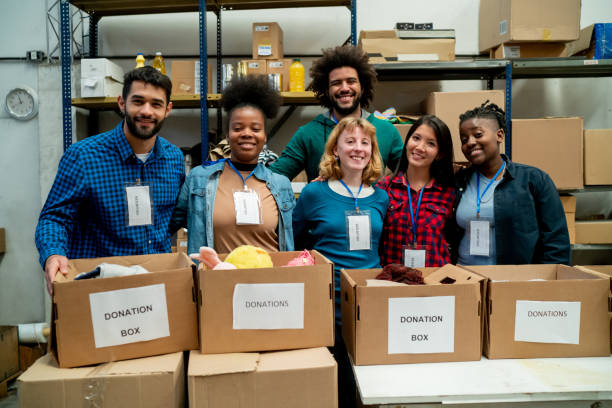 Large group of diverse volunteers at a charitable foundation standing behind a table with donation boxes facing camera smiling