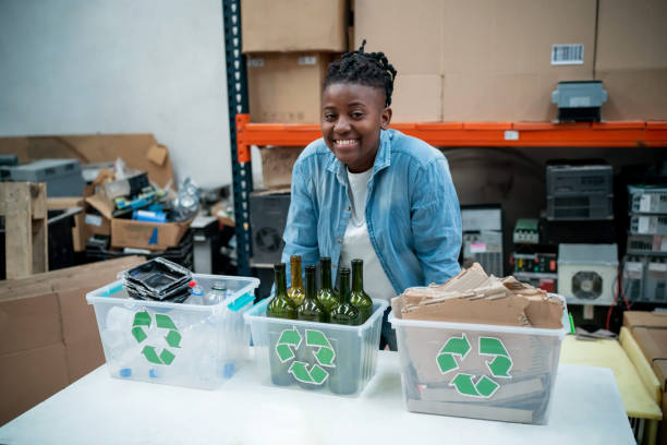 Cheerful black young female volunteer at a recycling centre facing camera smiling while leaning  her hands on table - Environmental conservation concepts