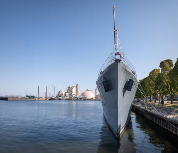 The bow and superstructure of HMAS Hobart, DDG-39, a Hobart Class destroyer of the Royal Australian Navy docked at Garden Island naval base in Sydney Harbour. On the left is a buoy used to allow ships to dock next to each other. In the left background is HMAS Warramunga, FFH-152, an Anzac Class frigate. This image was taken on a cold and sunny afternoon on 1 July 2024