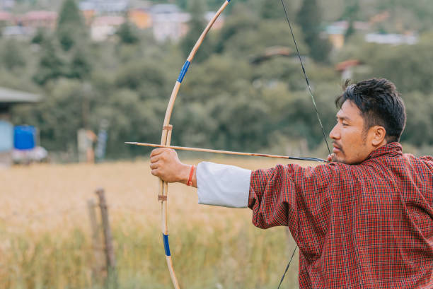 Bhutanese Man practicing archery aiming and shooting  in field Bhutanese Man practicing archery aiming and shooting  in field bhutanese culture photos stock pictures, royalty-free photos & images