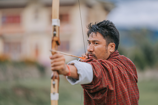 Bhutanese Man practicing archery aiming and shooting  in field