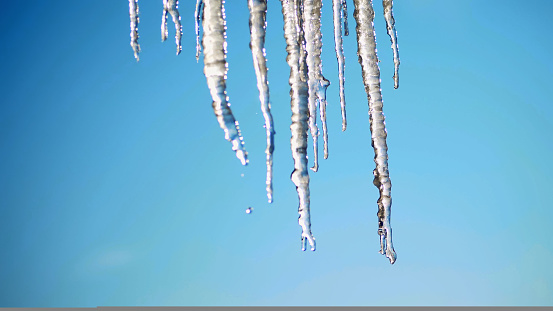 winter, frosty, snowy, sunny day. close-up, large transparent icicles hang from the roof, against the sky. High quality photo