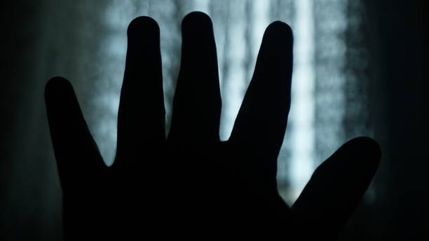 istock Hand silhouette on a dark room with blurred window background. Concept for Halloween day. Dark theme. 1435476778