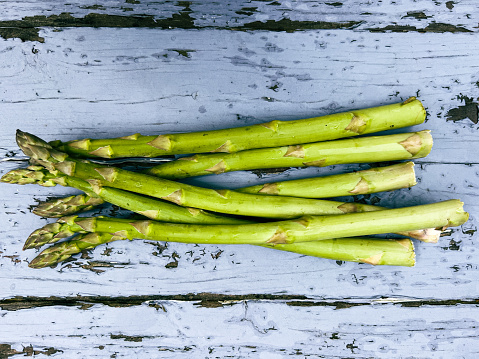 Horizontal closeup photo of a bunch of organic green Asparagus lying on a weathered pale blue painted wooden table in Spring.