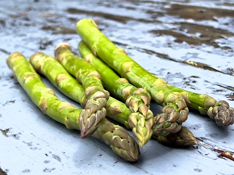 Horizontal extreme closeup photo of a bunch of organic green Asparagus lying on a weathered pale blue painted wooden table in Spring. Soft focus background.