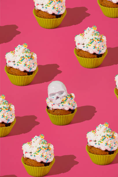 istock Halloween pattern with a muffin with whipped cream and a skeleton head against a pink background. Spooky Holiday food concept. 1435484468