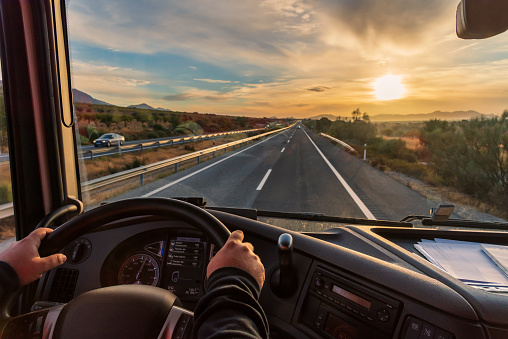 View from the driver's seat of a truck of the highway and a landscape of fields at dawn.