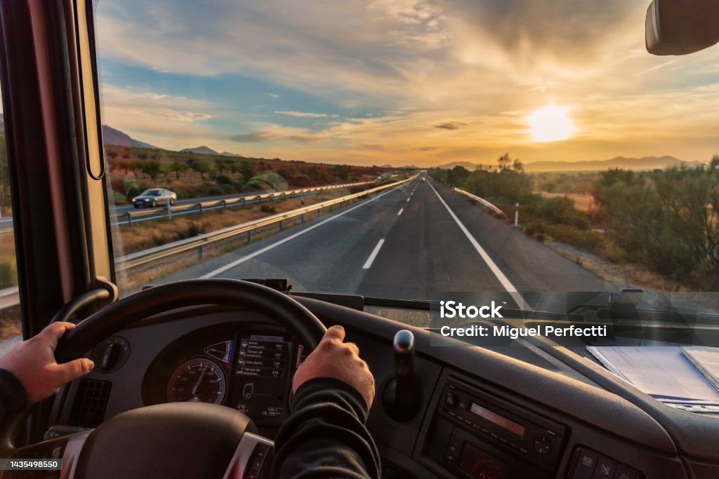 View from the driver's seat of a truck of the highway and a landscape of fields at dawn, with a dramatic sky. View from the driver's seat of a truck of the highway and a landscape of fields at dawn. Truck Stock Photo