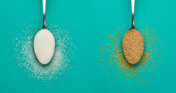 Brown and white sugar in a teaspoon scattered over a green background