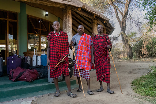 Tarangire, Tanzania - October 12th, 2022: Three masai tribesmen employed as porters in a savannah lodge in Tanzania, in traditional attire.