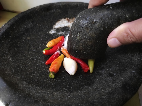 Puree cayenne pepper and garlic to make a traditional Indonesian chili sauce using a mortar and pestle.