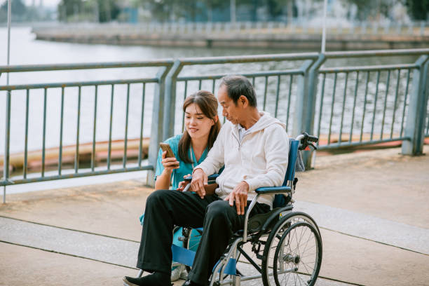 Nurse showing healthcare tips on mobile phone to senior patient while on wheelchair - concept of technology, support and caregiver stock photo