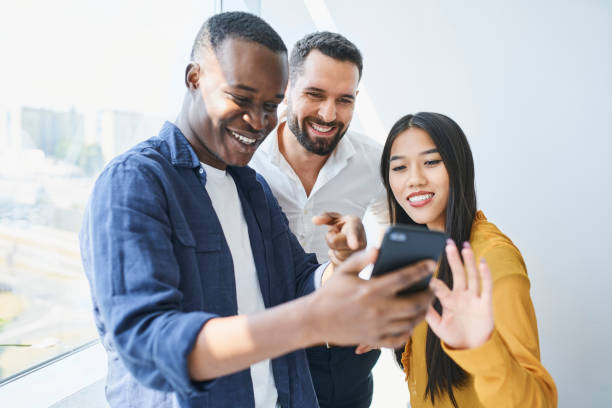 istock Happy coworkers looking at phone in office. Students share smartphone at university 1435516989