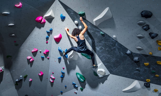 Sportswoman training climbing on indoor climbing wall Fit young woman climbing wall in gym. Sportswoman during intense climbing session in an indoor climbing centre. unyielding stock pictures, royalty-free photos & images