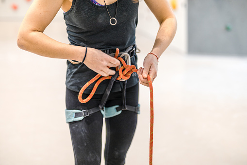 Close-up of a female rock climber tying rope to her safety harness at a rock climbing center. Female climber hands ties a safety knot on the harness before climbing the artificial wall.