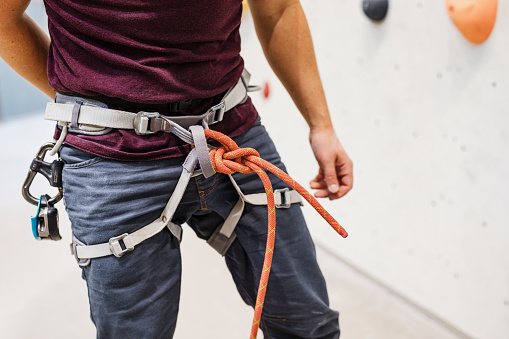 Mid section of male climber ready to climb indoor. Man wearing safety harness with a rope attached at indoors rock climbing center.