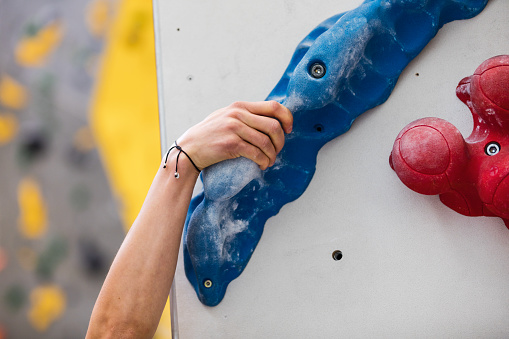Close-up of a strong woman reaches up to grip a crimp hold while lead climbing in a training center. Caucasian woman gripping a crimp hold on artificial rock climbing wall.