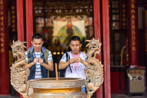 Asian Chinese gay couples hands holding joss sticks blessing in front of altar table at chinese shrine