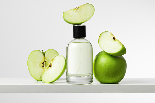 Female fragrance surrounded by fresh green apples in light studio closeup. Bottle with fruit perfume demonstration. Luxury cosmetic product advertisement