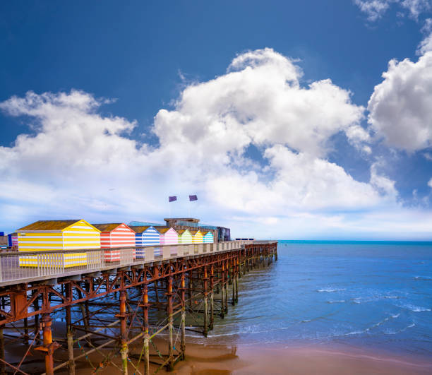 пляж и пирс гастингса красочные полосатые хижины курорт, восточный суссекс англия великобритания - sussex стоковые фото и изображения