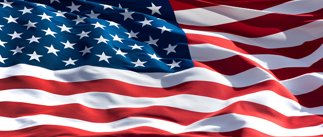 An American Flag hanging from a column on the front porch glows in the morning light as the sun rises.