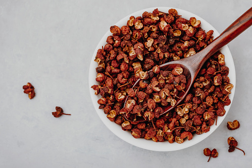 Sichuan pepper. Chinese pepper (Zanthoxylum schinifolium) in bowl on gray stone background. Top view with copy space. Dried spices, Food Ingredients.