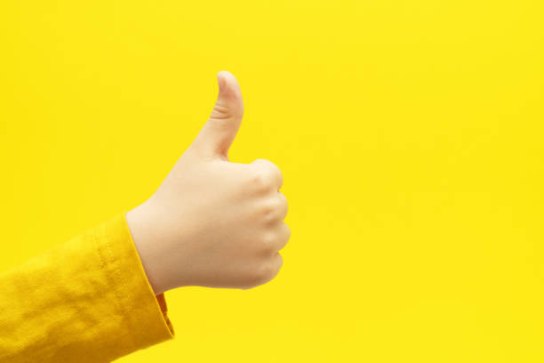 istock Child hand with thumb up gesture on bright yellow background. Like sign. 1435523741