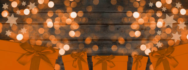 Festive Christmas background banner template greeting card - Orange gift boxes, stars and sparkles bokeh lights isolated on abstract dark black anthracite grey gray wooden texture