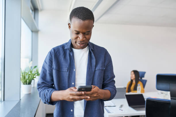 istock Young African American man using phone at office. Male entrepreneur browsing internet on smartphone in co working office space 1435530735