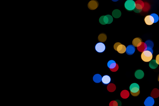 Colorful blurred lighs bokeh on black background as a festive backdrop, night defocused light spots