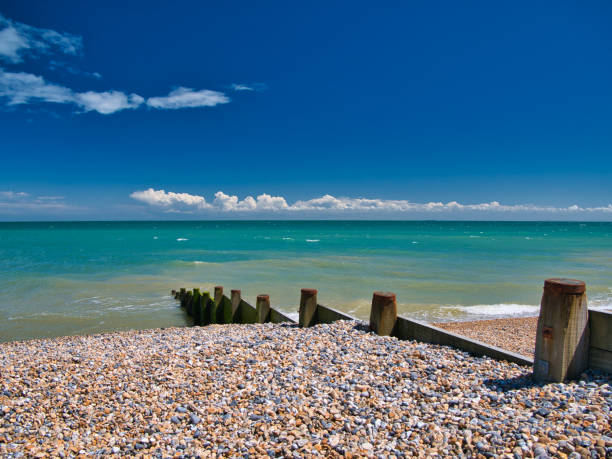 A wooden breakwater on the shingle beach in Kingsdown in Kent. Taken on a clear, sunny day with a blue sky, light cloud and a turquoise sea. A wooden breakwater on the shingle beach in Kingsdown in Kent. Taken on a clear, sunny day with a blue sky, light cloud and a turquoise sea. groyne stock pictures, royalty-free photos & images
