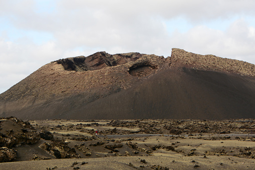 Lanzarote, parque natural de los volcanes: surrounding with lava plain and single Caldera de los Cuervos volcano. In the middle two unrecognizable tourists.