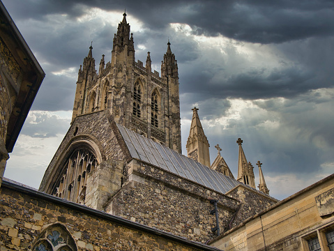 The stone towers of Canterbury Cathedral in Kent, UK with a background of an overcast sky with heavy grey clouds.