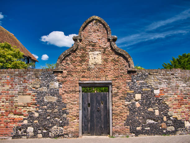 An old wooden gate surrounded by an arch of rustic brickwork and stone facing on both sides. A plaque on the left is inscribed The Kings Lodging - Strand Street, Sandwich.