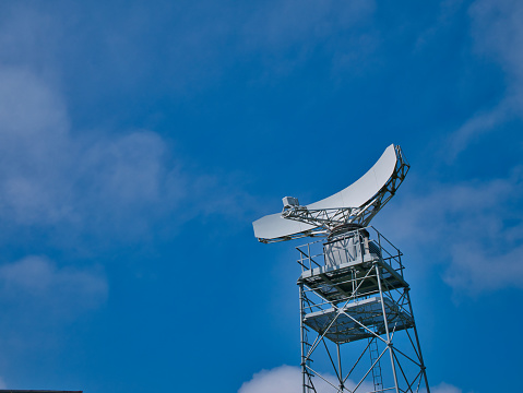 A white radar dish mounted on a steel frame tower. Taken on a sunny day in Summer.