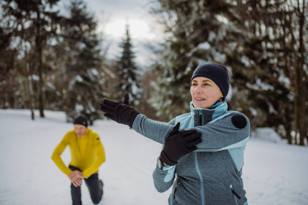 Senior couple warming-up and stretching in snowy forest before winter hike. stock photo