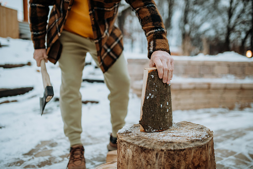 Low section of man chopping wood outdoor during snowy winter day.