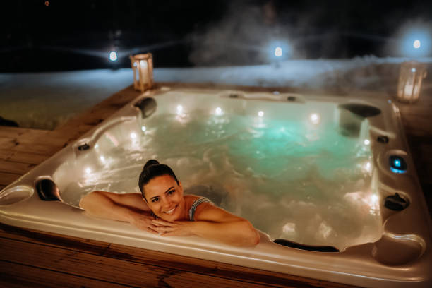 молодая женщина наслаждается ванной на открытой террасе холодным зимним вечером. - whirlpool стоковые фото и изображения