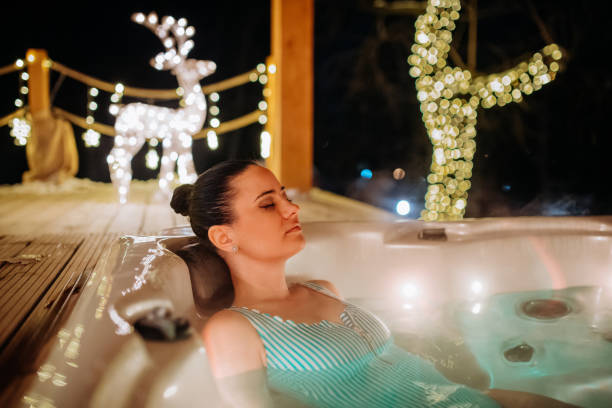 Young woman enjoying outdoor bathtub in her terrace during cold winter evening. stock photo