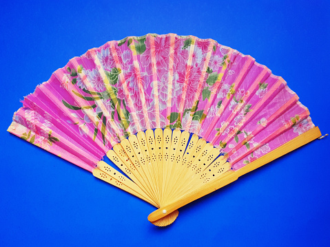 An old hand-crafted fan that is starting to break down, made of bamboo blades and strips of patterned pink cloth