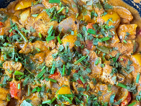 Stock photo showing chicken breast chunks in a pan tikka masala curry sauce and chopped coriander leaves.