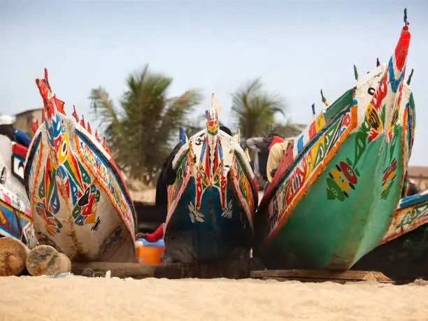 The painted decorative bows of 3 fishing boats, known as Pirogues, on the sandy beach in the fishing village of Tanji on the Atlantic coast of Gambia in tropical West Africa. Good copy space.