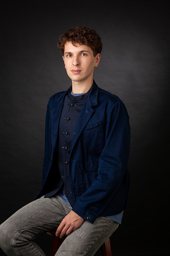 Studio portrait of a young white man in a blue jacket on a black background